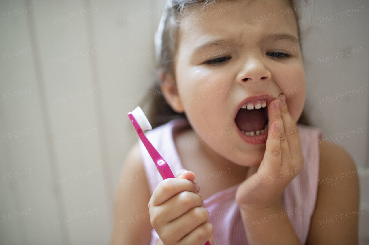 Front view portrait of worried small girl with toothbrush indoors, loosing baby tooth.