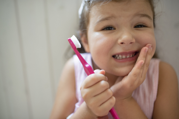 Front view portrait of worried small girl with toothbrush indoors, loosing baby tooth.