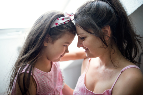 Portrait of mother and small daughter indoors at home, hugging.