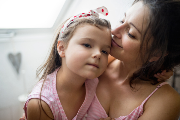 Portrait of mother and small daughter indoors at home, hugging.