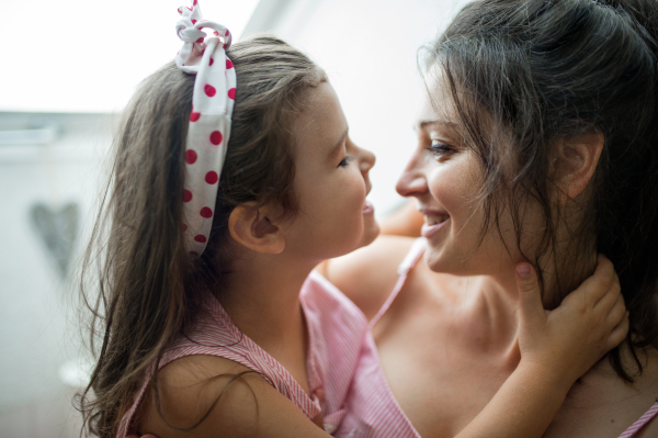 Portrait of mother and small daughter indoors at home, hugging.