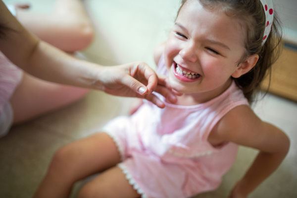 Top view of crying small girl with unrecognizable mother indoors, loosing baby tooth.