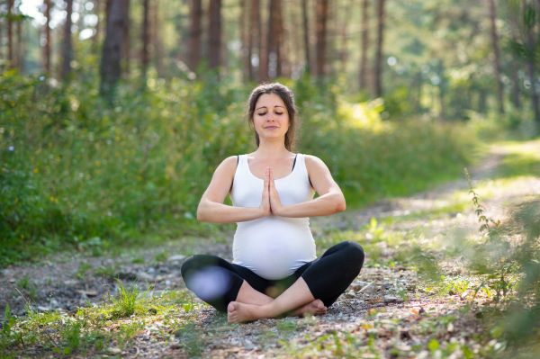 Front view portrait of happy pregnant woman outdoors in nature, doing yoga exercise.