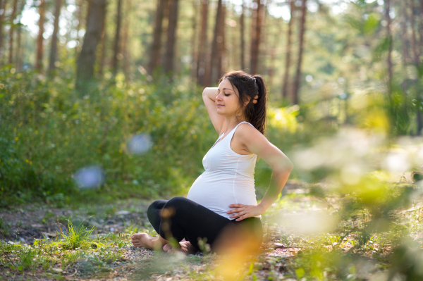 Front view portrait of happy pregnant woman outdoors in nature, doing yoga exercise.