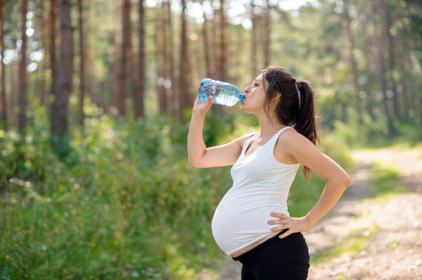 Side view of pregnant woman outdoors in nature, drinking water after doing exercise.