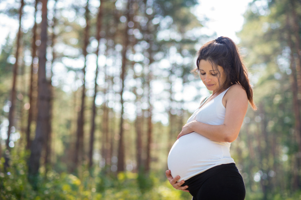 Side view portrait of happy pregnant woman outdoors in nature, touching her belly.