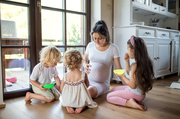 Happy pregnant woman with small children indoors at home, talking.