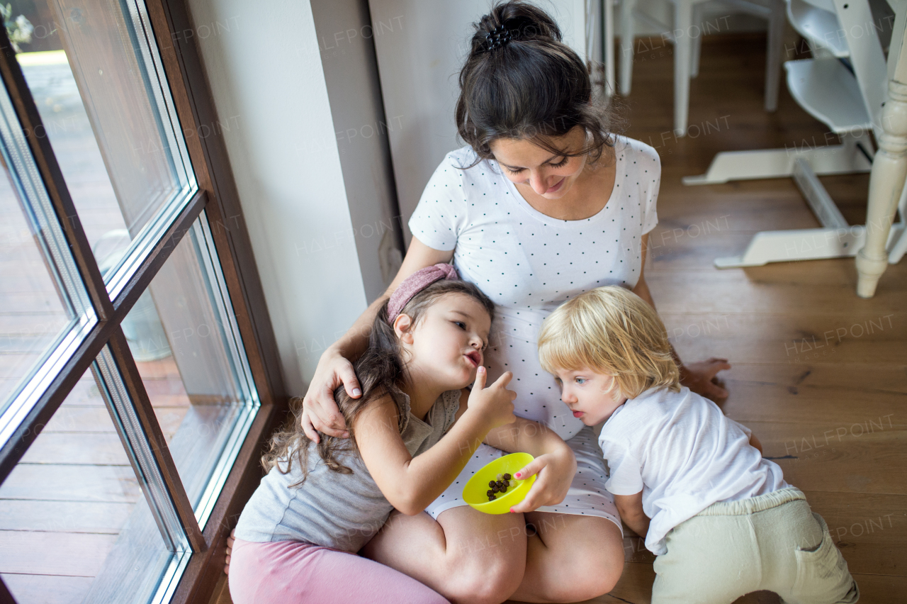 Top view of small children hugging pregnant belly of mother expecting baby indoors at home.