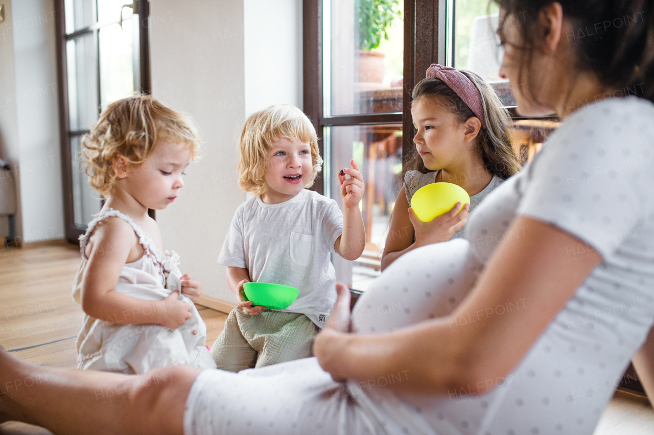 Happy pregnant woman with small children indoors at home, eating biscuits.