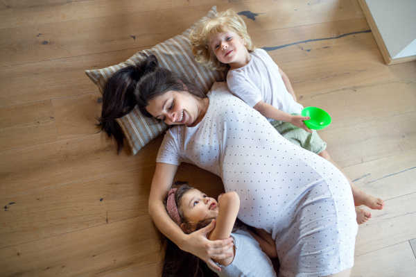 Top view of happy pregnant woman with small children indoors at home, lying on floor.