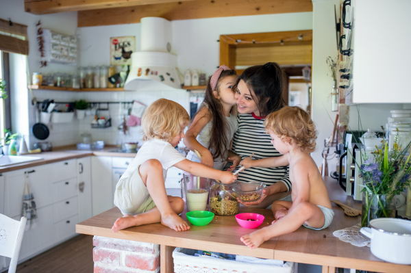 Happy pregnant woman with three small children indoors at home, preparing breakfast.