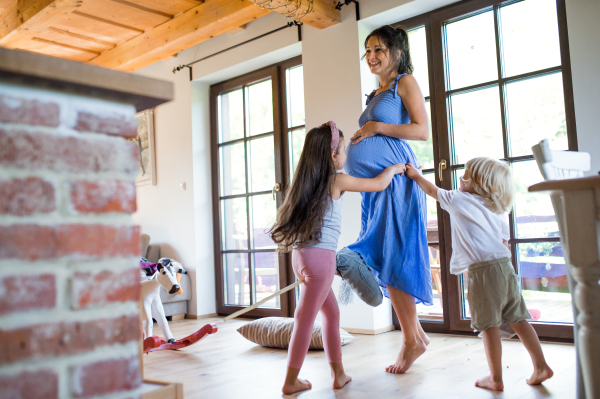 Happy pregnant woman with small children indoors at home, playing.