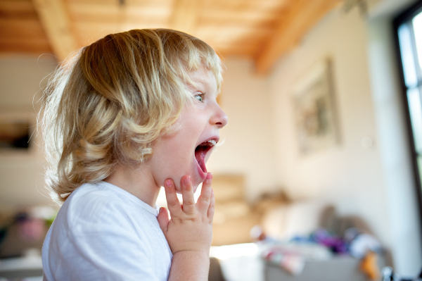 Side view portrait of small boy with open mouth indoor at home.