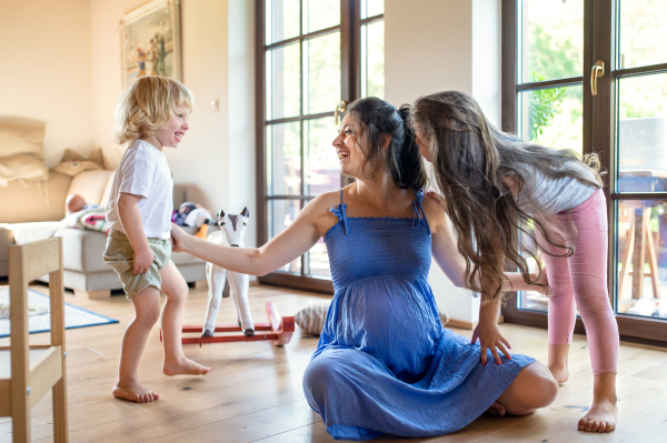 Happy pregnant woman with small children indoors at home, playing.