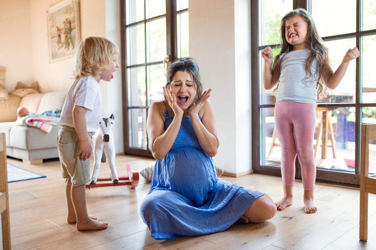 Unhappy pregnant woman with screaming small children indoors at home, feeling hopeless.