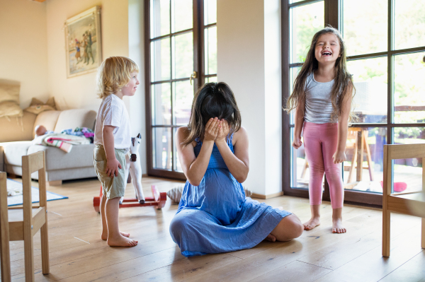 Unhappy pregnant woman with screaming small children indoors at home, feeling hopeless.