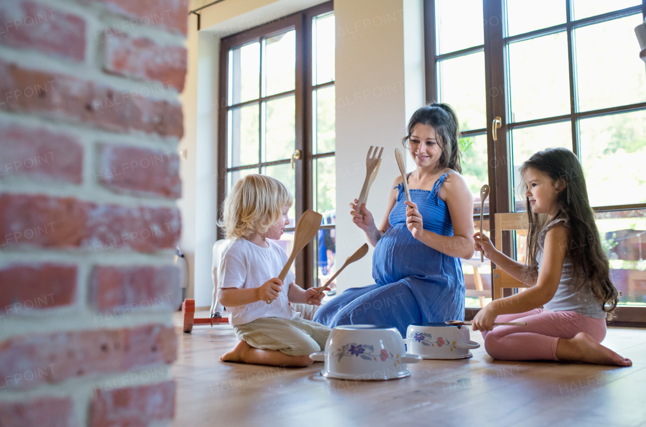 Happy pregnant woman with small children indoors at home, playing.