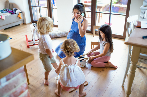 Happy pregnant woman with small children indoors at home, using smartphone.