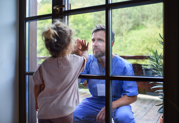 Doctor coming to see and greet family in isolation, window glass separating them.