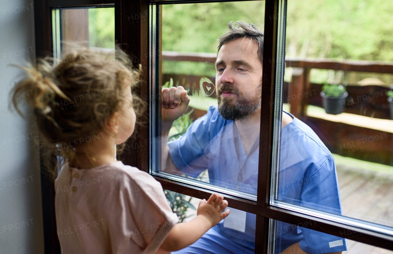 Doctor coming to see and greet daughter in isolation, window glass separating them.