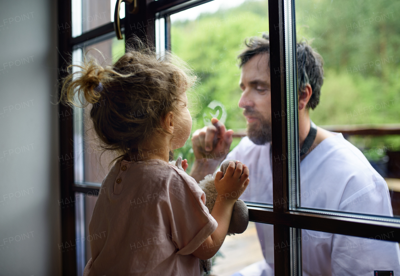 Doctor coming to see and greet family in isolation, window glass separating them.