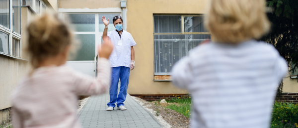 Sad children greeting father doctor from distance in front of hospital, coronavirus concept.