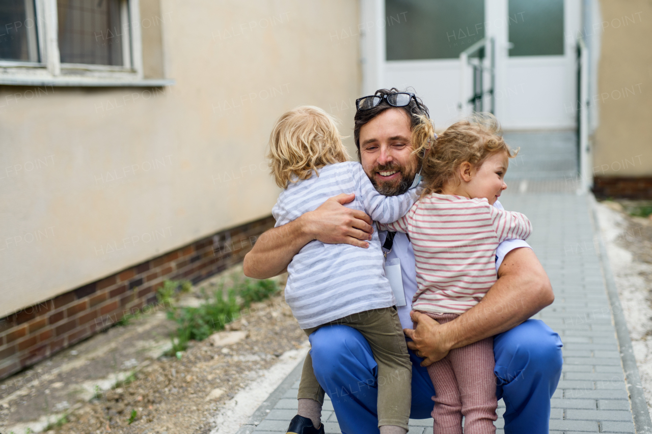 Happy children greeting father doctor in front of hospital, end of coronavirus concept.