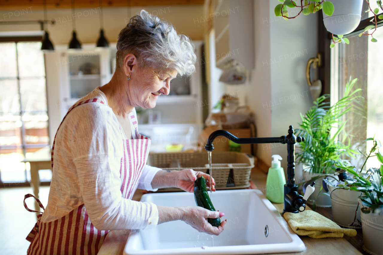 Side view of woman washing vegetables indoors at home when cooking, corona virus concept.