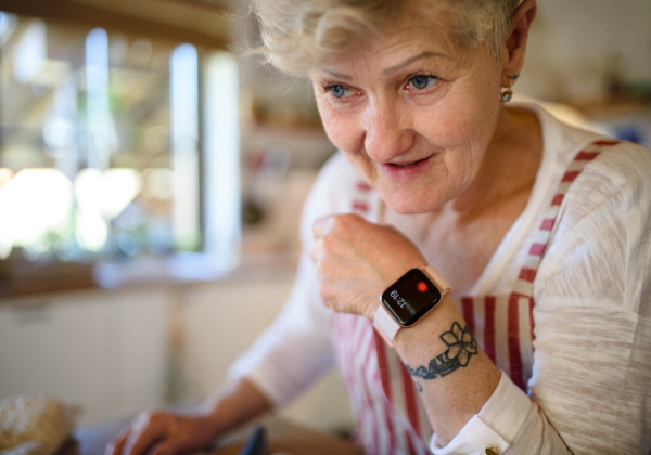 Close-up of senior woman with apron and smartwatch indoors at home.