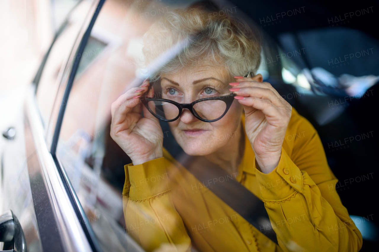 A senior woman with glasses sitting in a car. Shot through glass.