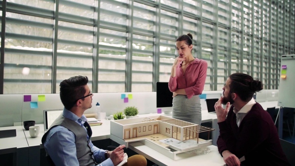 A group of young architects with model of a house in office, working and talking. Slow motion.