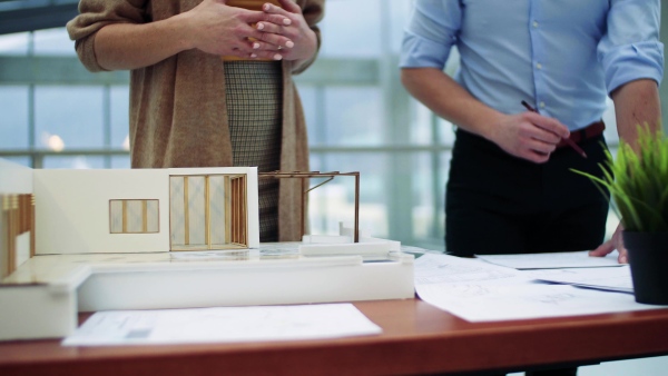 Midsection of two architects with model of a house standing in office, talking.