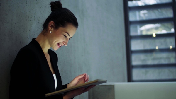 A young business woman with tablet standing in office, working.