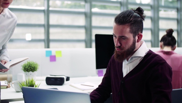 A group of young businesspeople with laptop working in office, talking.