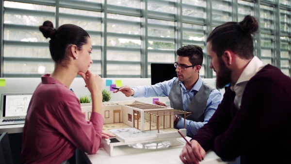 A group of young architects with model of a house in office, working and talking.