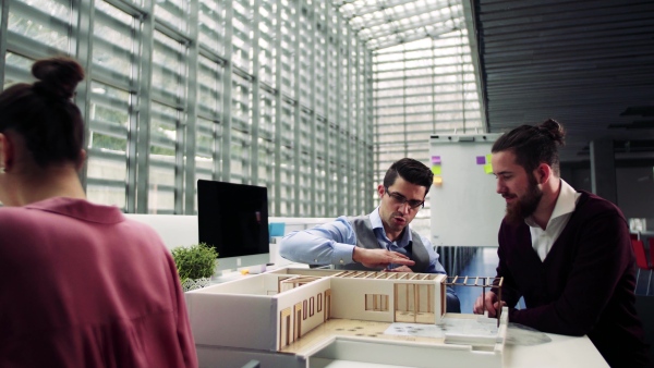 A group of young architects with model of a house in office, working and talking.