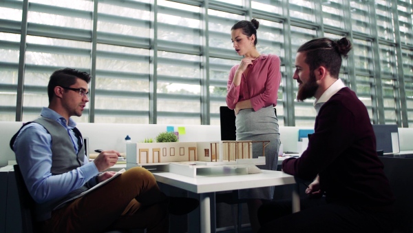 A group of young architects with model of a house in office, working and talking.