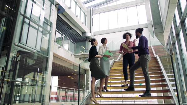 A group of young businesspeople standing on a staircase, talking.