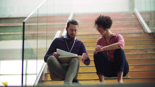 Two young businesspeople sitting on a staircase, talking. Slow motion.