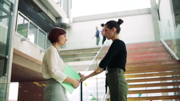 Two young businesswomen standing by a staircase, talking. Slow motion.