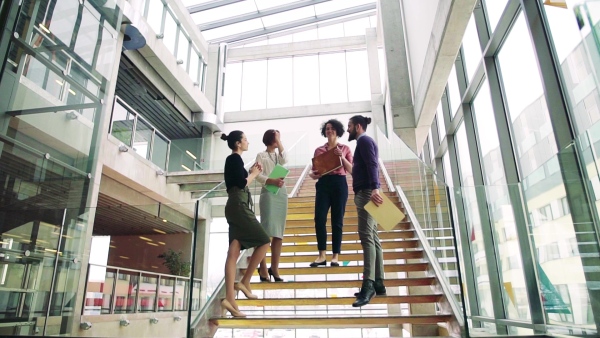 A group of young businesspeople standing on a staircase, talking. Slow motion.