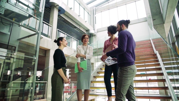 A group of young businesspeople standing by a staircase, talking. Slow motion.