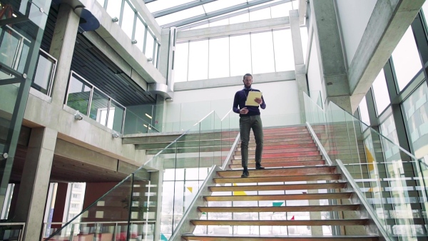 A young hipster businessman walking down the stairs in office building. Slow motion.