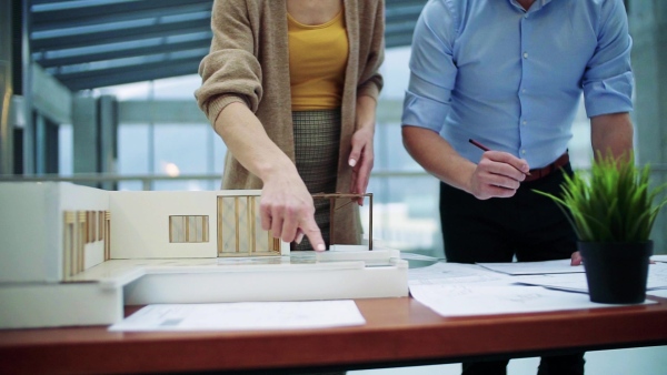 Midsection of two young architects with model of a house standing in office, working and talking. Slow motion.