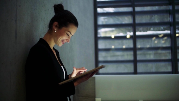 A young business woman with tablet walking in office, concrete wall in background. Slow motion.