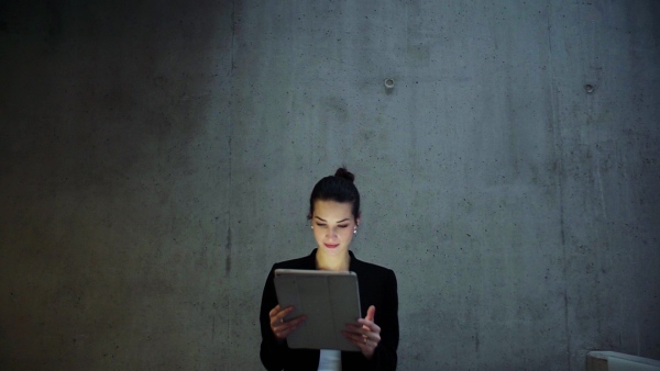 A young business woman with tablet walking in office, concrete wall in background. Slow motion.