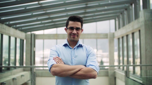 A portrait of young businessman standing indoors in an office. Slow motion.