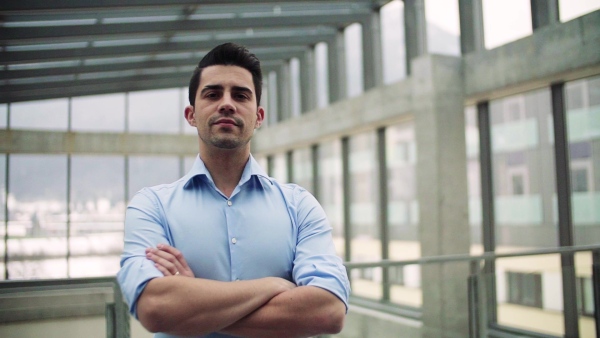 A portrait of young businessman standing indoors in an office. Slow motion.