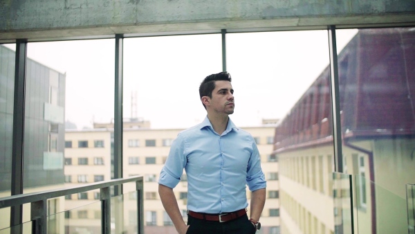 A portrait of young businessman walking indoors in an office, hands in pockets. Slow motion.