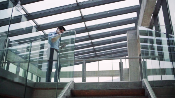 A young businessman with smartphone in corridor outside office, making a phone call. Slow motion.